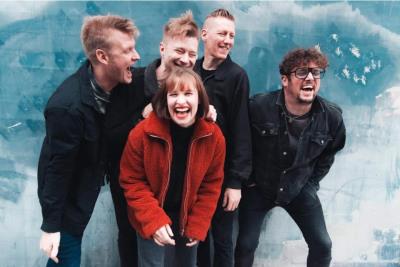 a group of four men and one woman in a red jacket, laughing and joking together