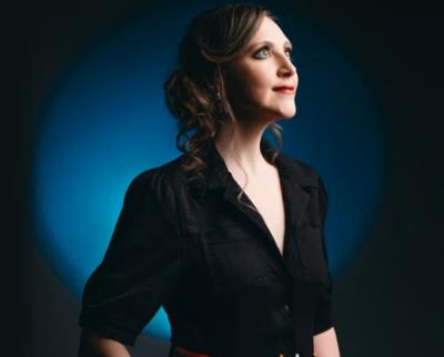 Portrait of Siobhan Miller wearing dark v neck blazer, with blue circle spotlight, wearing her hair up and in curls