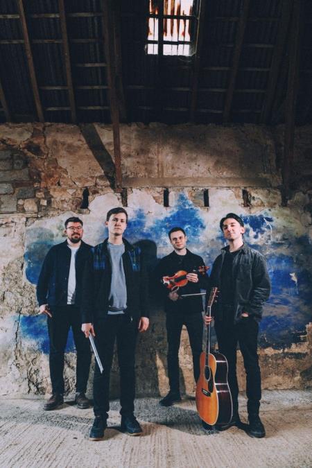 four men from the GNOSS band standing in front of dilapidated wall, holding musical instruments